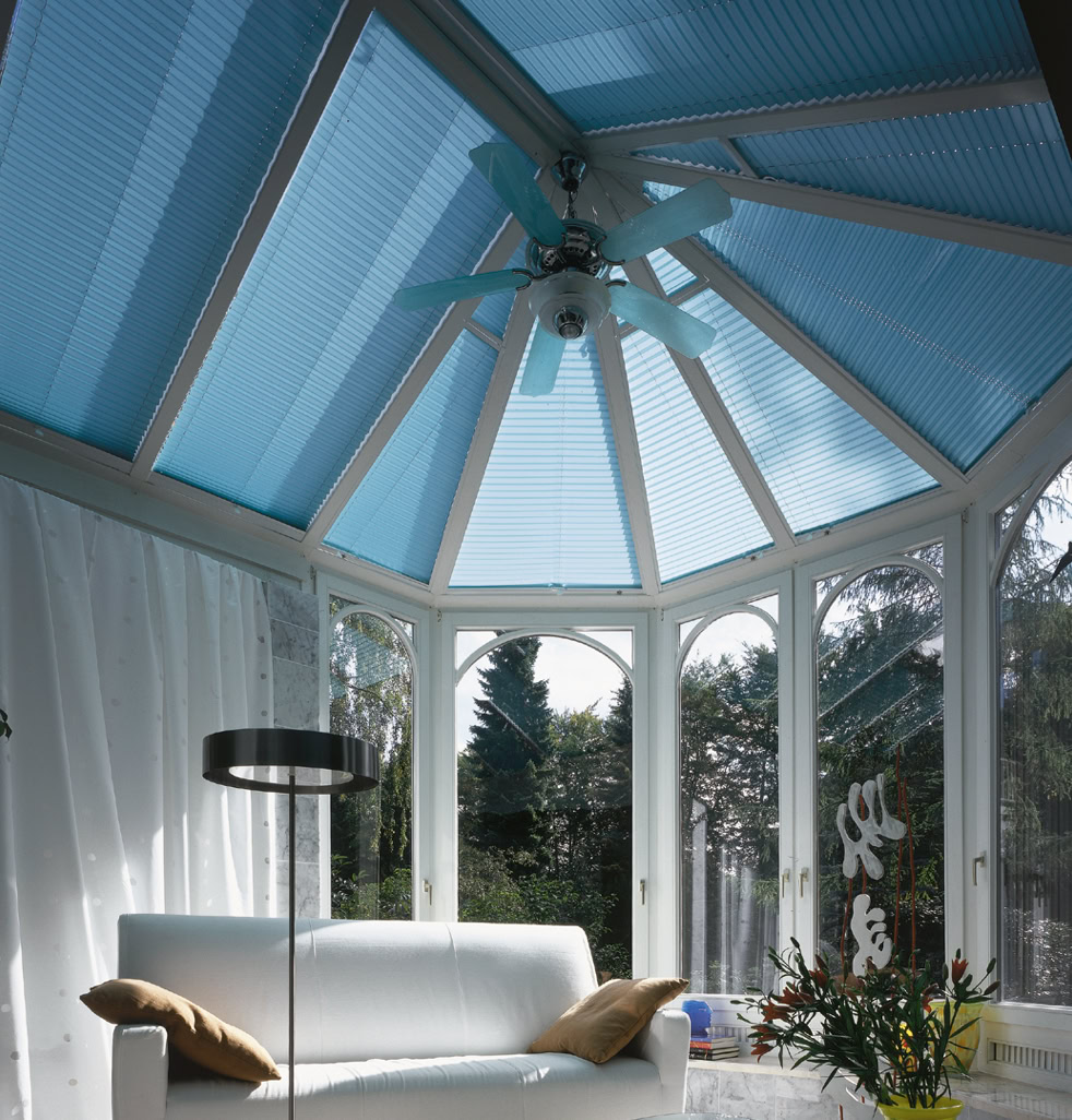 Wintergarten mit blauem Glasdach, weißem Sofa, Stehlampe und Pflanzen.